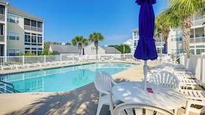 A pool area with white chairs and a table, surrounded by a white fence, and a blue umbrella. - 2 Mi to Beach: Grand Strand Condo w/ Pool Access! (North Myrtle Beach)