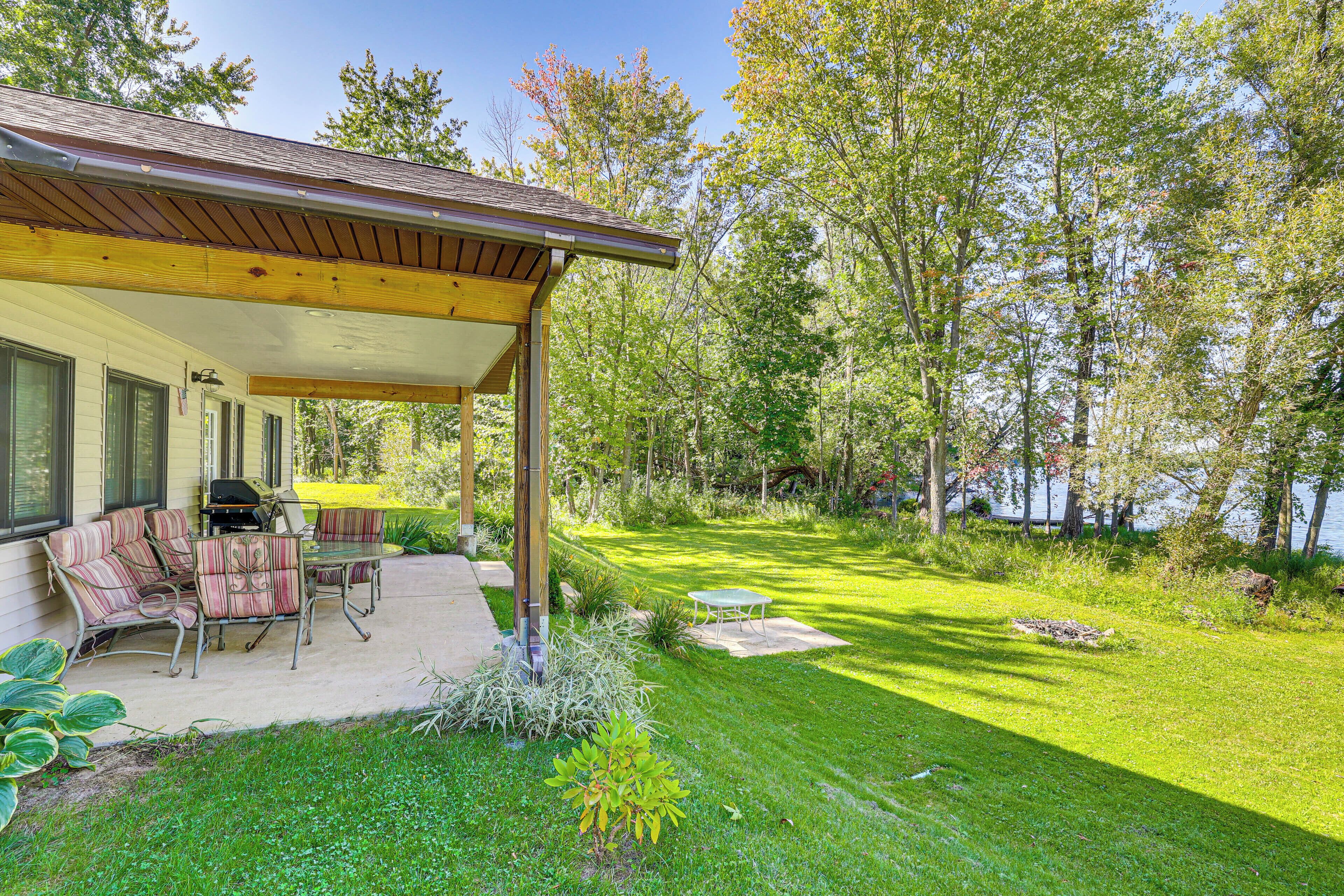 A covered patio with outdoor furniture, a grill, and a well-maintained lawn.