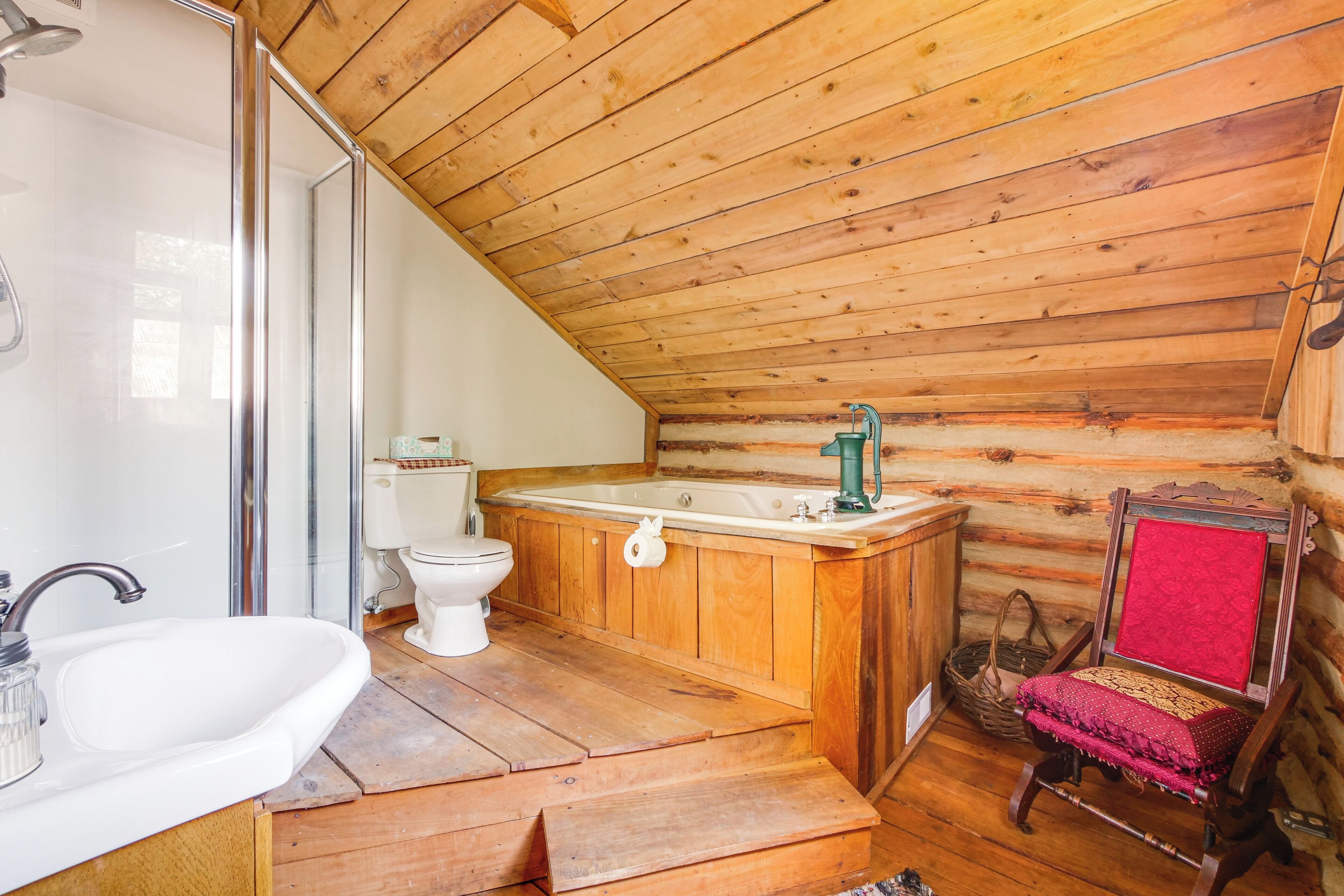 Une salle de bain rustique, aménagée dans une cabane en bois, comprenant une douche, un lavabo, des toilettes et une baignoire.