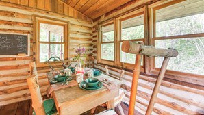 A rustic wooden cabin interior with a dining table set for four, a chalkboard with messages, and a large window with a view of trees. - 1800s Romantic Cabin! Fireplace + 3 Jacuzzi Tubs (Paris)
