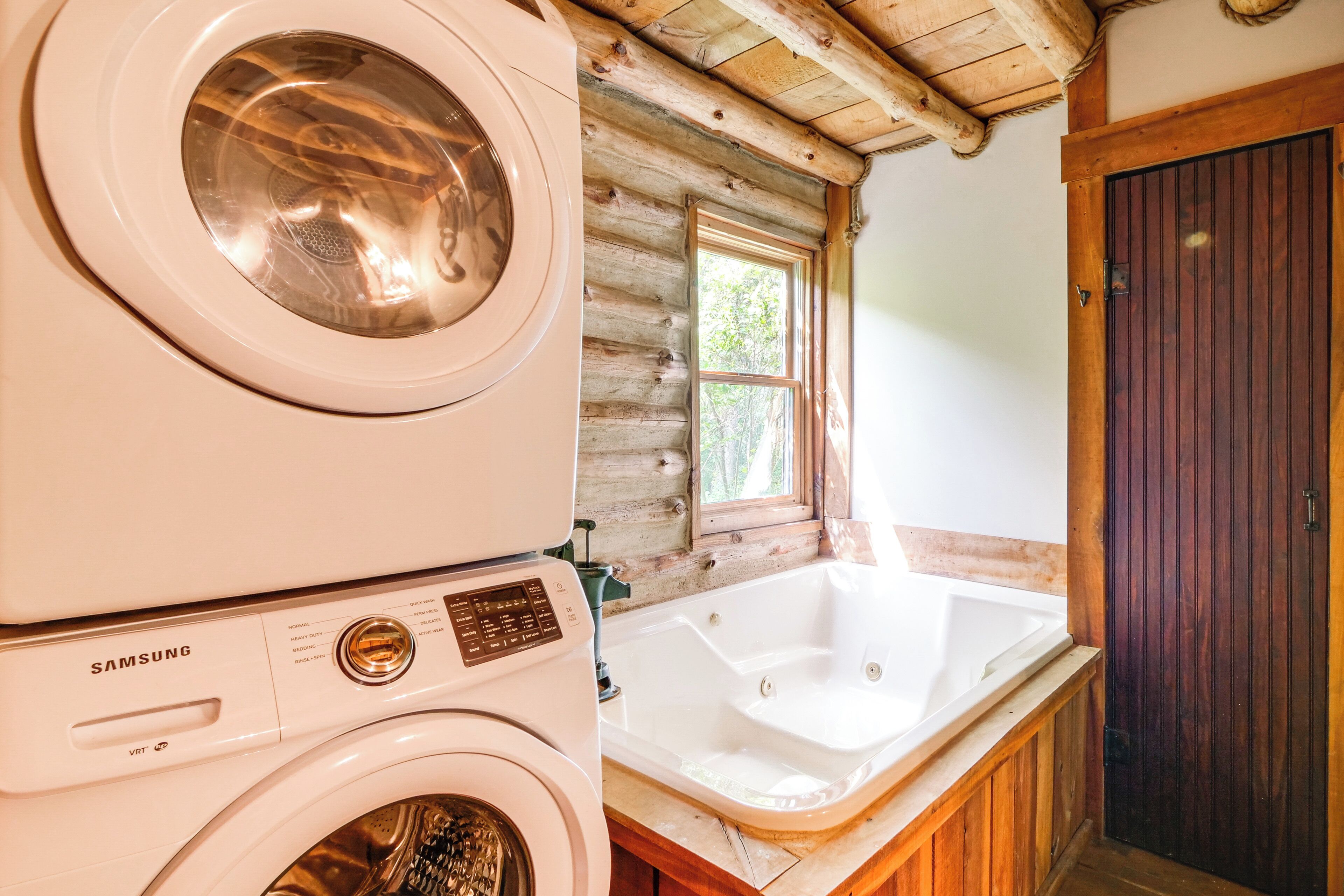 Ein Waschbereich mit einer Samsung Waschmaschine und einem Trockner, ein rustikales Holzhütten-Interieur und eine große Badewanne.