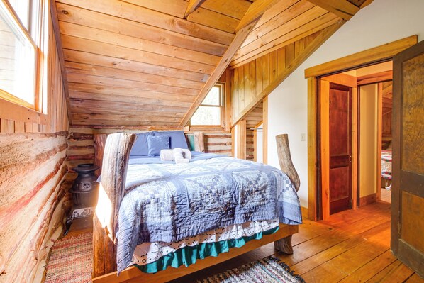 Une chambre mansardée chaleureuse avec un plafond en bois, un lit recouvert d’une couette bleue et blanche, un plancher en bois et un petit radiateur.