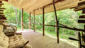A wooden deck with a cushioned seating area and a view of a forest. - 1800s Romantic Cabin! Fireplace + 3 Jacuzzi Tubs (Paris)