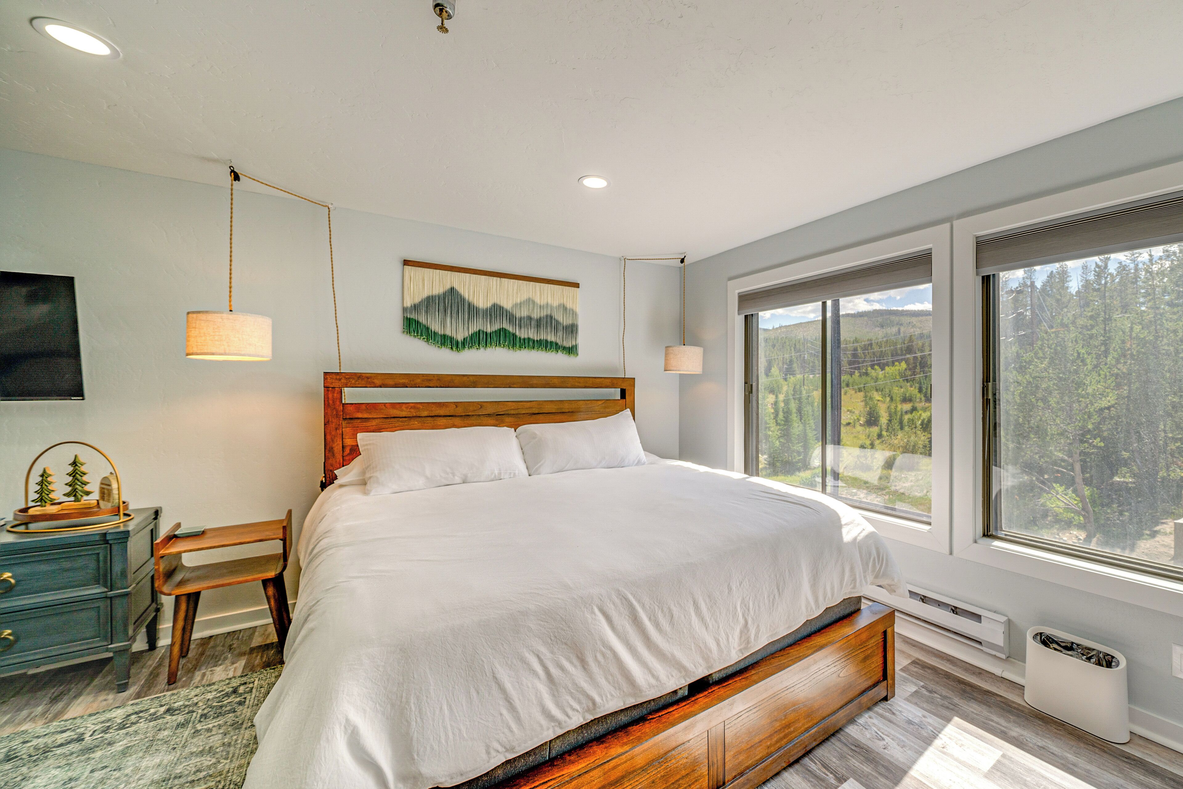 A bedroom with a large bed, wooden headboard, and a view of a forest through large windows.