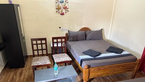 Une petite pièce comprenant un lit, deux chaises, une petite table et un réfrigérateur.