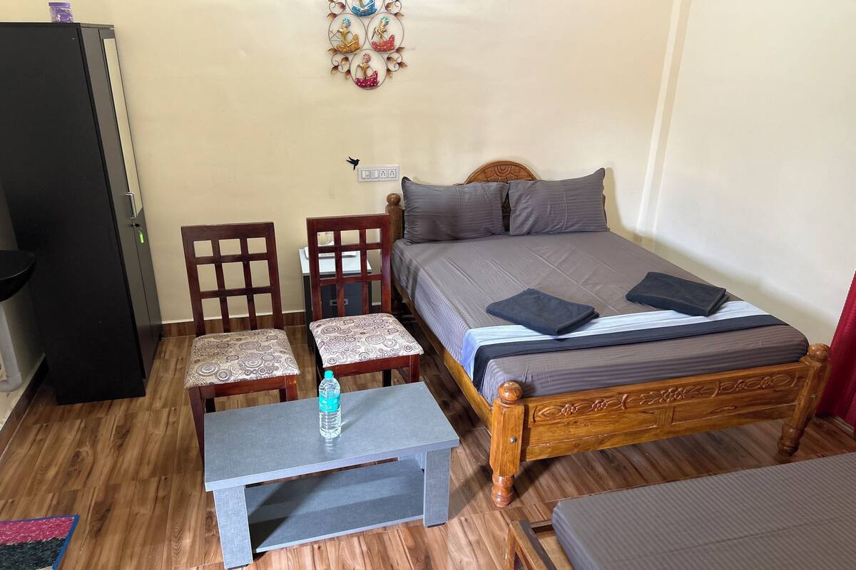 A compact room with a bed, two chairs, a small table, and a refrigerator.