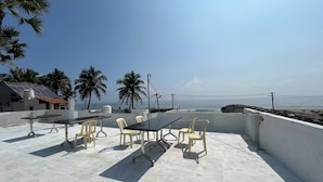 Une terrasse sur le toit, avec une table et des chaises, d’où l’on a vue sur une plage et des palmiers.