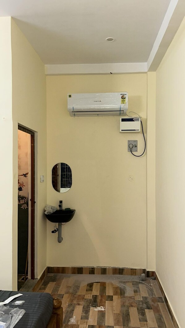 A small room with a tiled floor, a wall-mounted sink, a mirror, and an air conditioning unit. - Le'SAP Beach Resort (Vanur)
