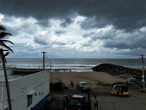 A coastal view with a beach, rocky area, and a building with a white facade. - Le'SAP Beach Resort (Vanur)