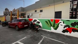 Un espace de stationnement avec une voiture rouge et une moto, un bâtiment orné d’une fresque murale et un ciel dégagé.