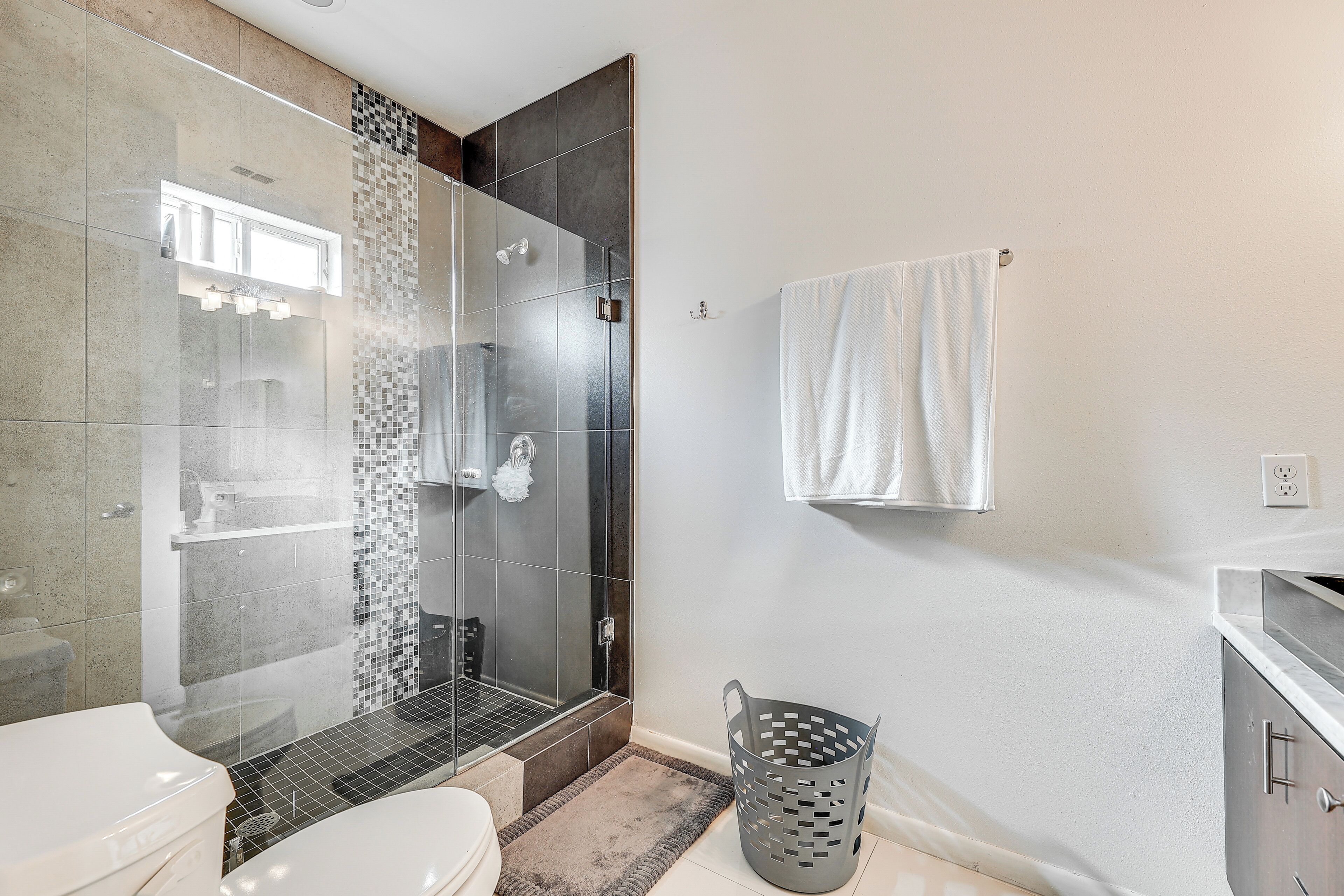 A modern bathroom with a glass shower enclosure, a toilet, a sink, and a towel hanging on the wall.