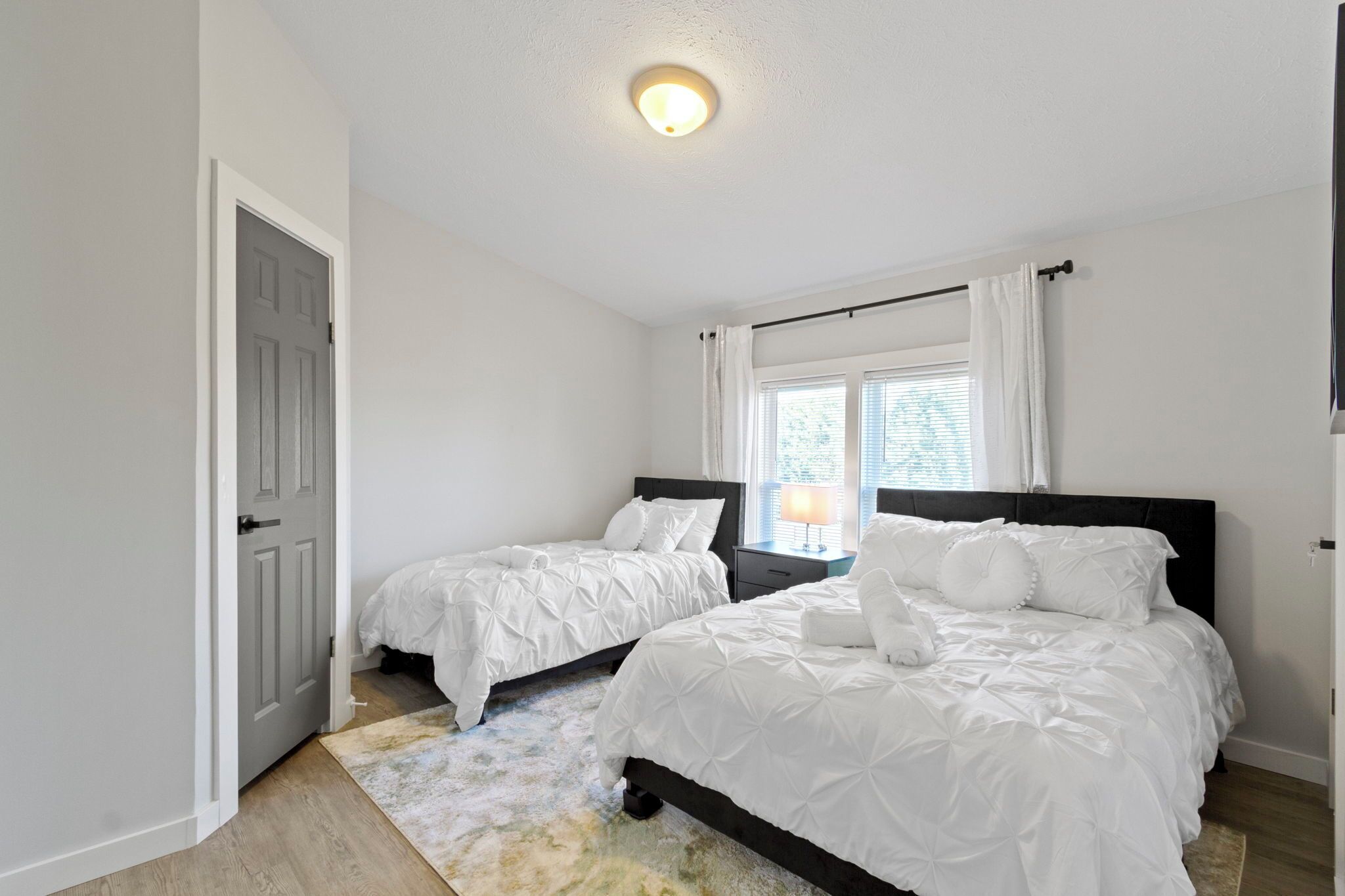 A bedroom with two beds, a nightstand, a window with curtains, and a ceiling light.