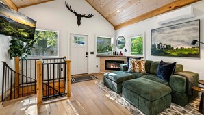 Ein gemütliches Wohnzimmer mit Kamin, einem grünen Sofa, Holzboden und einer Dekoration mit einem Hirschschädel.
