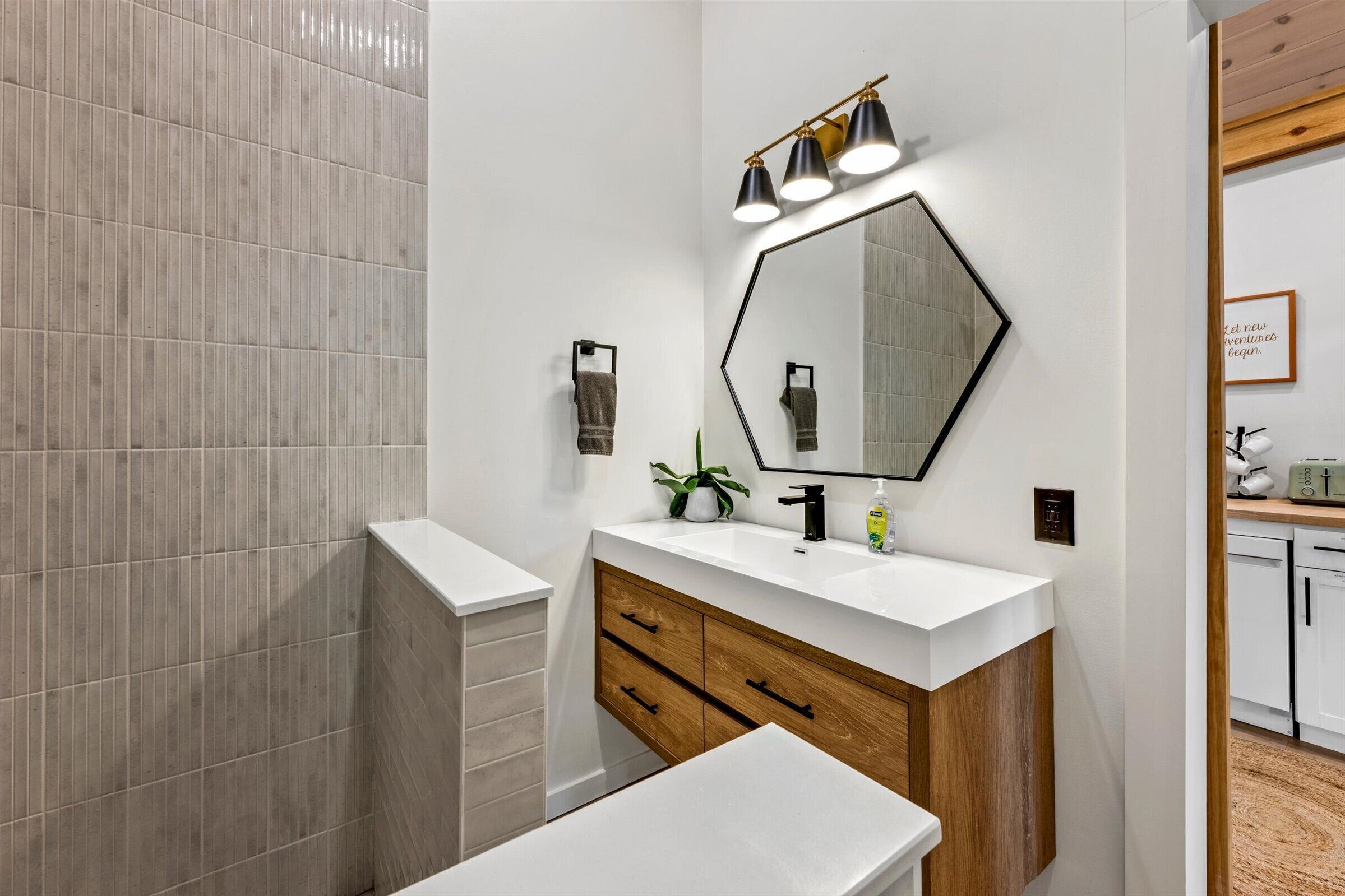 Een moderne badkamer met een witte wastafel, een spiegel met geometrisch kader, en een douchehoek.