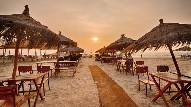A beachside restaurant with thatched umbrellas and wooden tables and chairs. - Royale Amata By the Beach (Morjim)