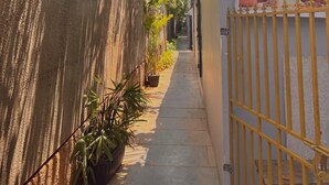 A narrow alley with a concrete wall on one side and a yellow gate on the other. There are potted plants along the wall and a sign for 'flora wellness center' with a phone number. - Royale Amata By the Beach (Morjim)