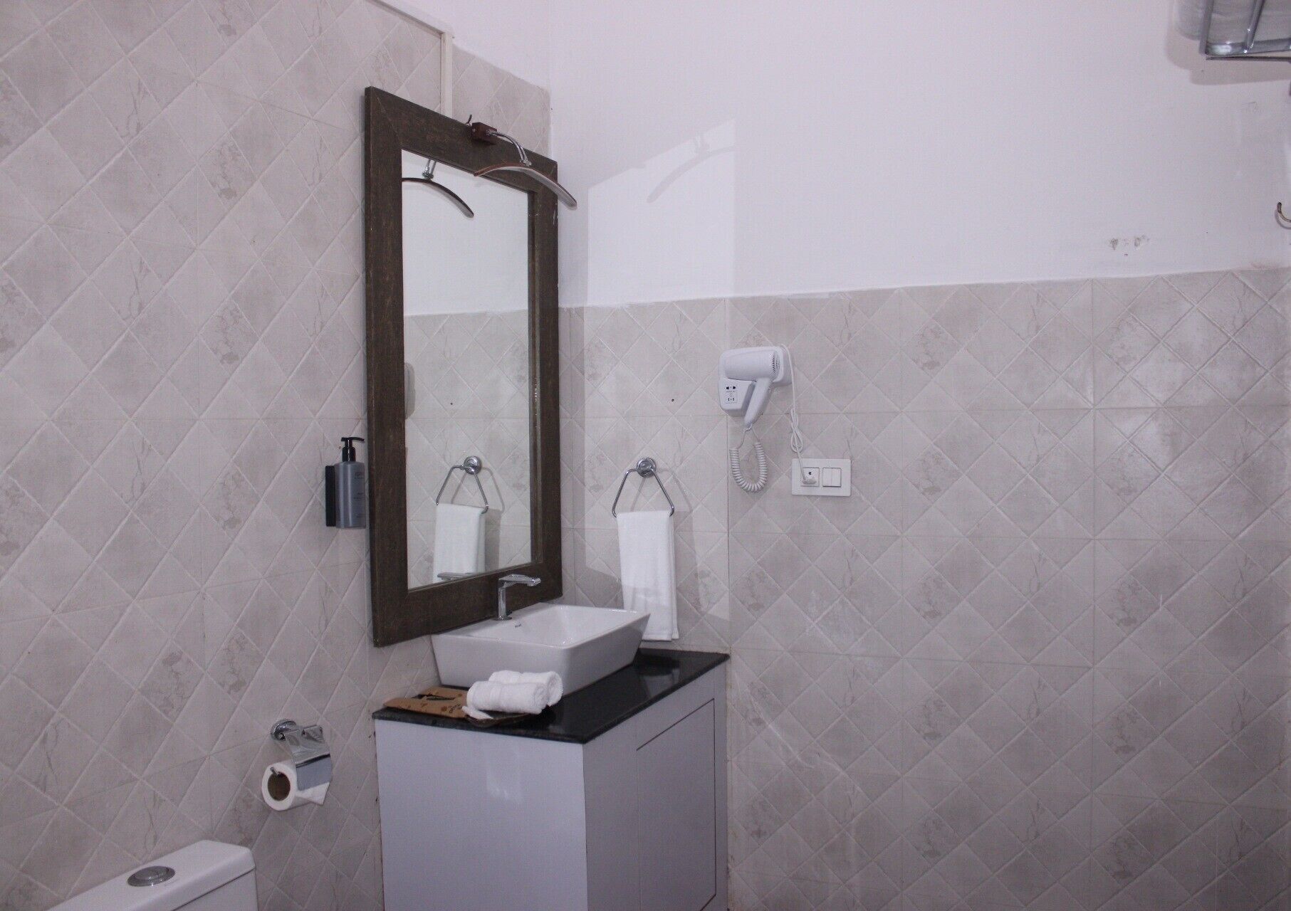 A bathroom with a sink, mirror, towel rack, toilet, and a hairdryer on the wall.
