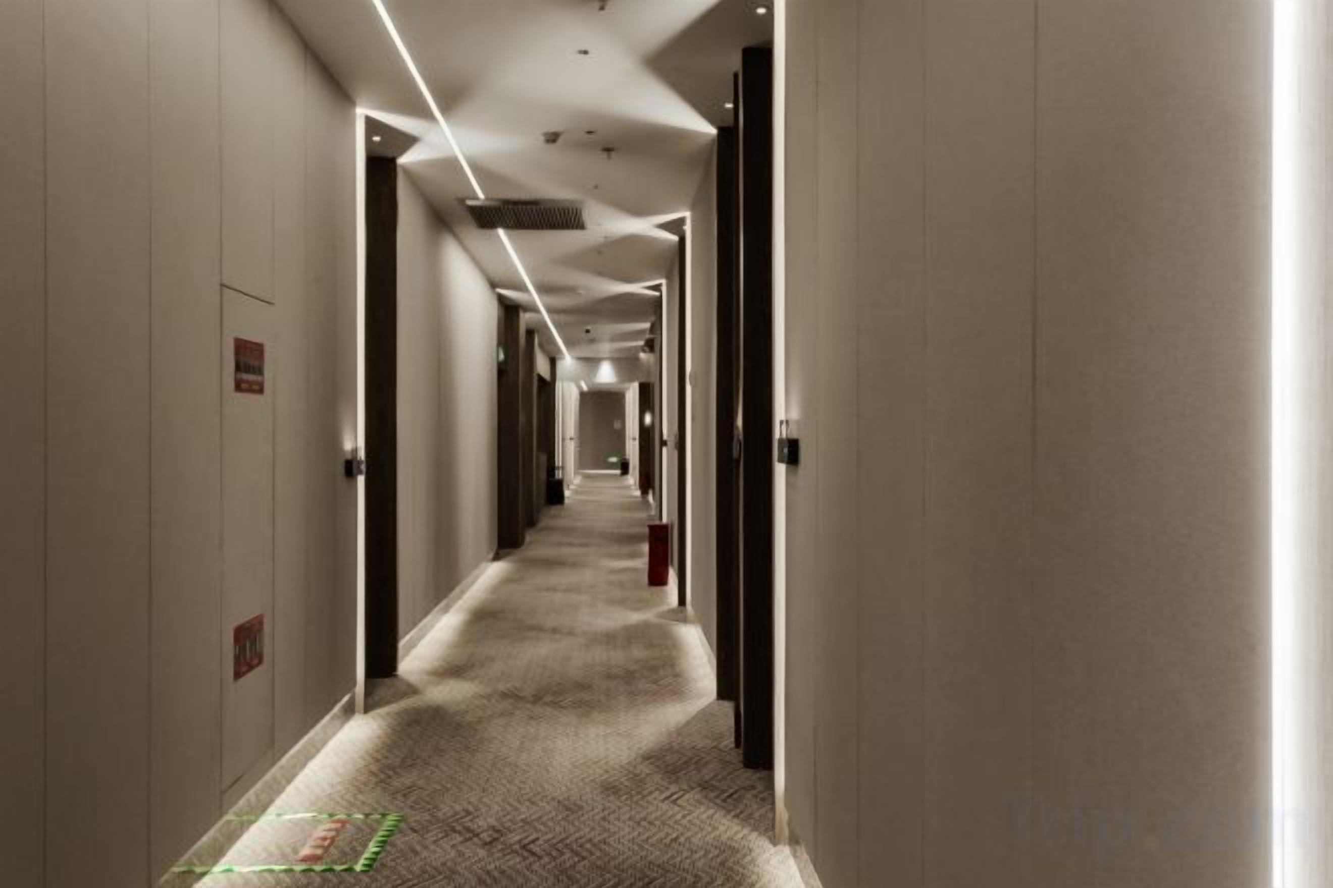 Een hotelgang met deuren aan beide kanten, voorzien van vloerbedekking en verlichting in het plafond.