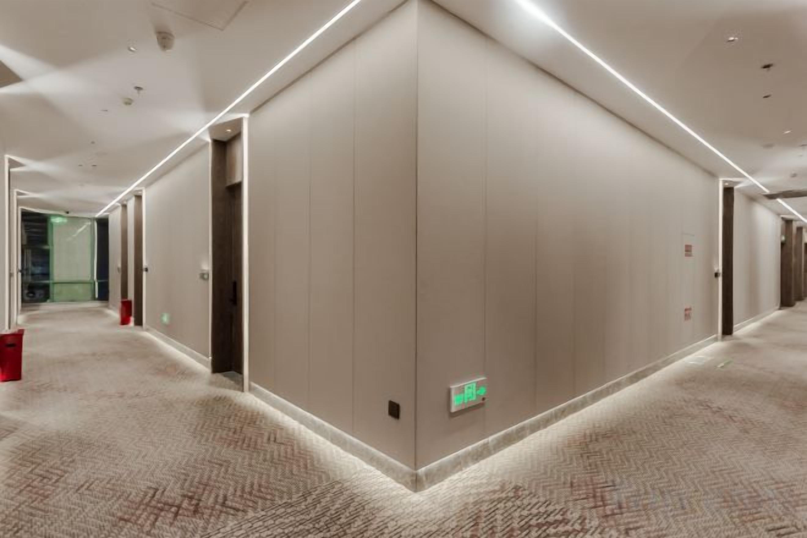 A hotel corridor with carpeted floors, doors, and emergency exit signs.