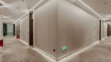 A hotel corridor with carpeted floors, doors, and emergency exit signs.