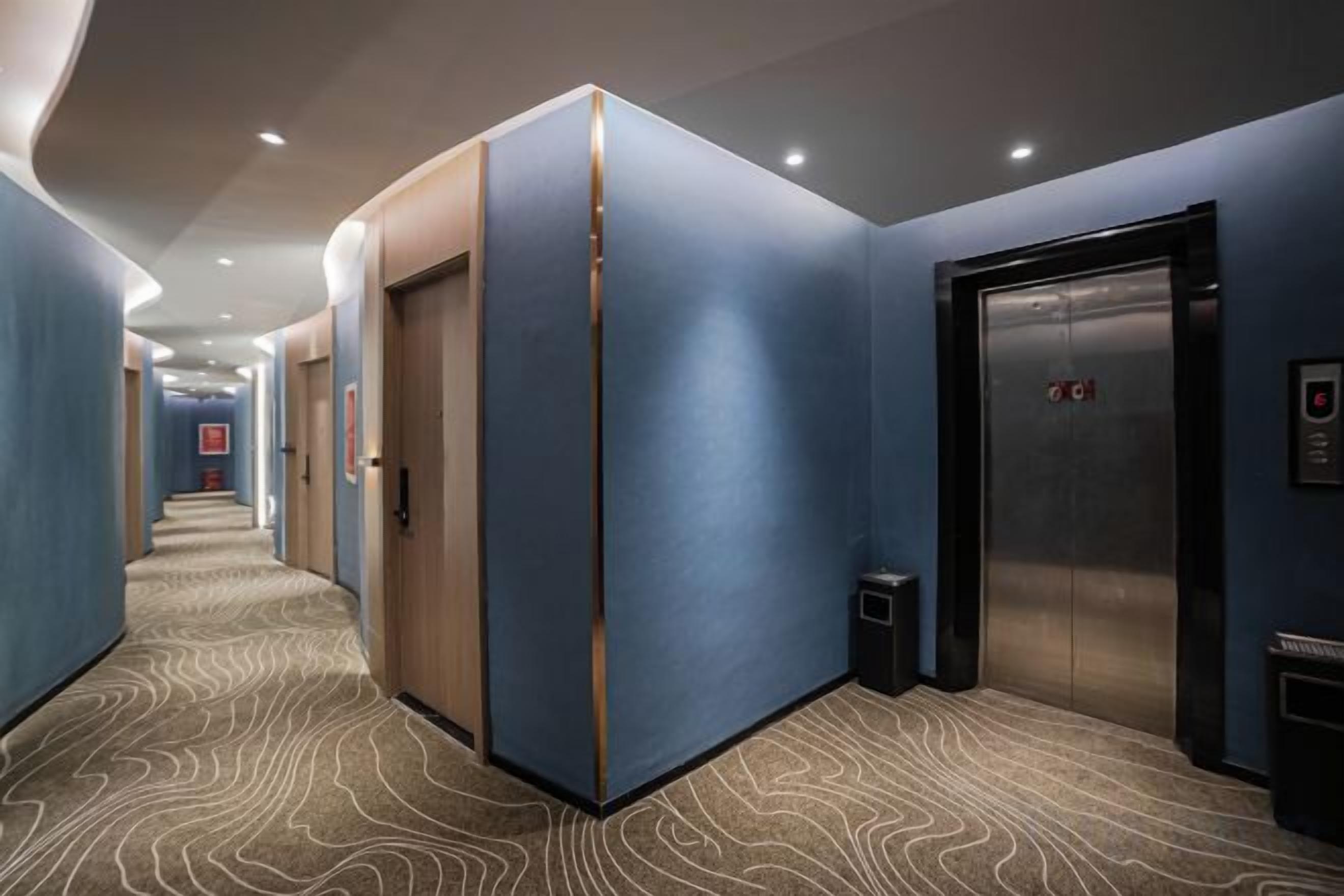 A hotel corridor with a carpeted floor, a wooden door, and an elevator.