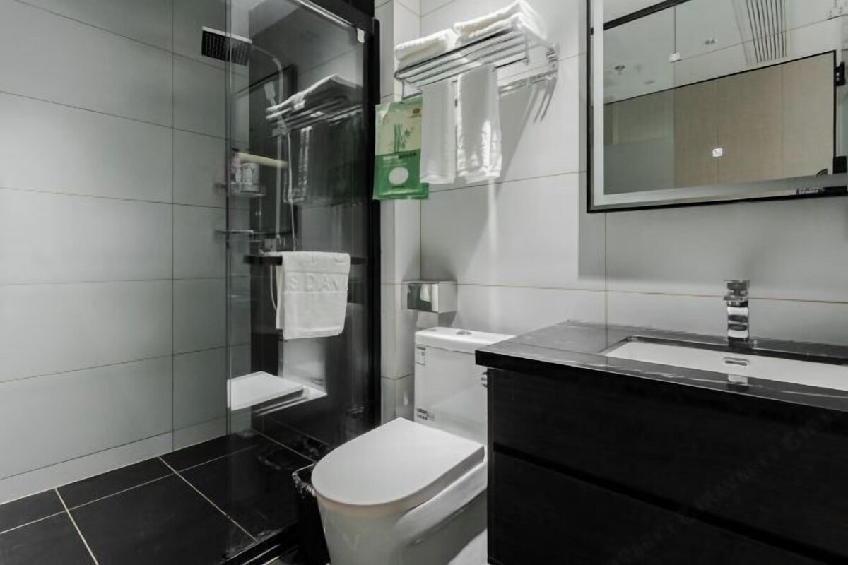 A modern bathroom with a glass shower enclosure, a white toilet, a black vanity with a mirror, and a towel rack with folded towels.