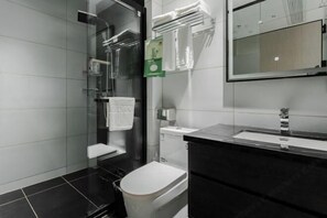 A modern bathroom with a glass shower enclosure, a white toilet, a black vanity with a mirror, and a towel rack with folded towels.