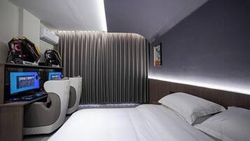 Una habitación de hotel moderna con una cama curvada, un escritorio con computadora y un amplio ventanal con cortinas.