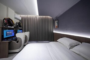 A modern hotel room with a curved bed, a desk with a computer, and a large window with curtains.