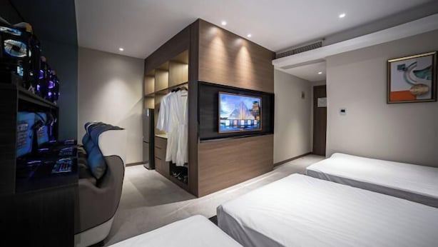 Una camera d'albergo con televisore, postazione per videogiochi, due letti e cabina armadio.