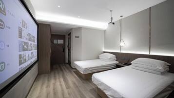 Habitación de hotel con dos camas, una pantalla grande mostrando imágenes y suelo de madera.