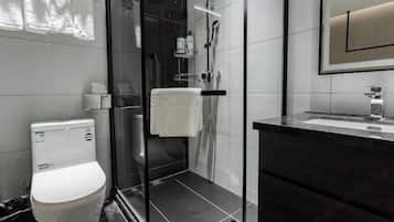 Un baño moderno con ducha de vidrio, inodoro blanco y tocador oscuro con espejo.