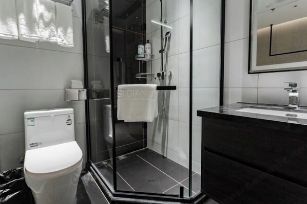 A modern bathroom with a glass-enclosed shower, a white toilet, and a dark-toned vanity with a mirror.