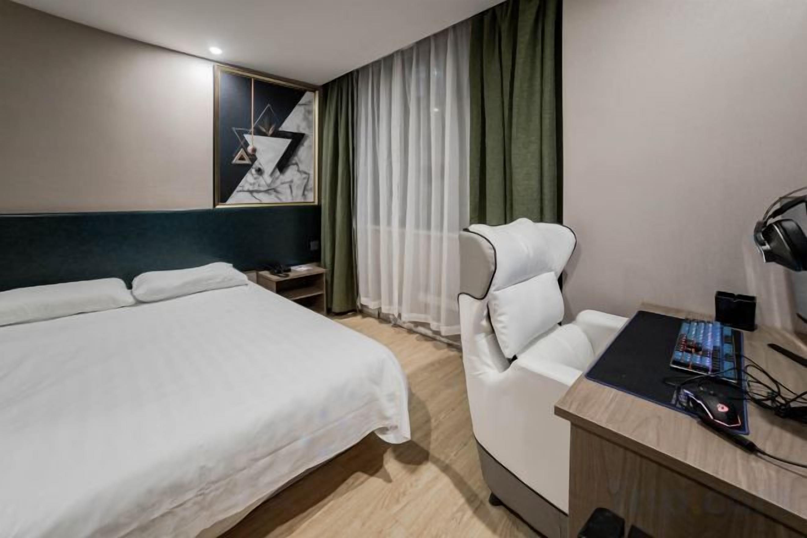 Et hotelværelse med seng, skrivebord med computer og stol.