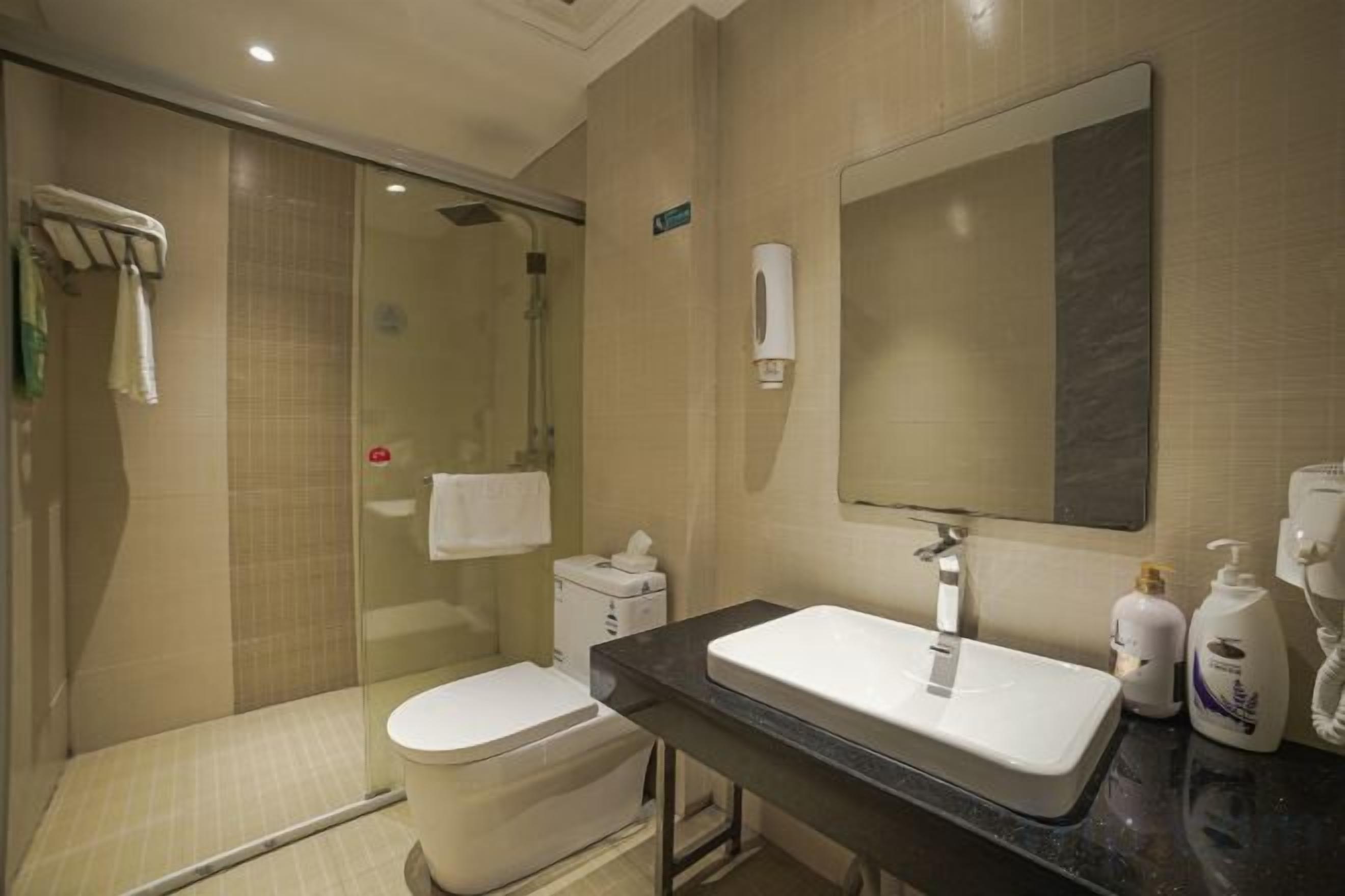 Une salle de bain d’hôtel avec une douche à parois de verre, des toilettes, un lavabo et un miroir.