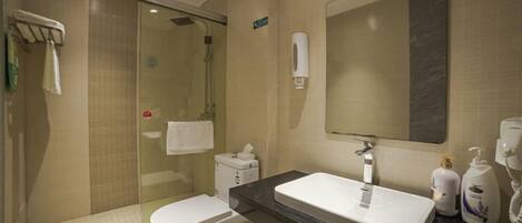 Une salle de bain d’hôtel avec une douche à parois de verre, des toilettes, un lavabo et un miroir.