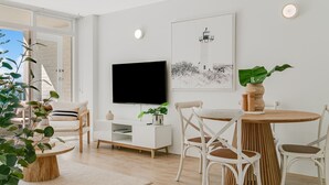 A modern living room with a flat-screen TV, a dining table with chairs, a potted plant, and a framed picture on the wall. - Rainbow Pacific Unit 4 - Oceanfront Unit in Rainbow Bay, Coolangatta Linen and Wi-Fi included (Coolangatta)