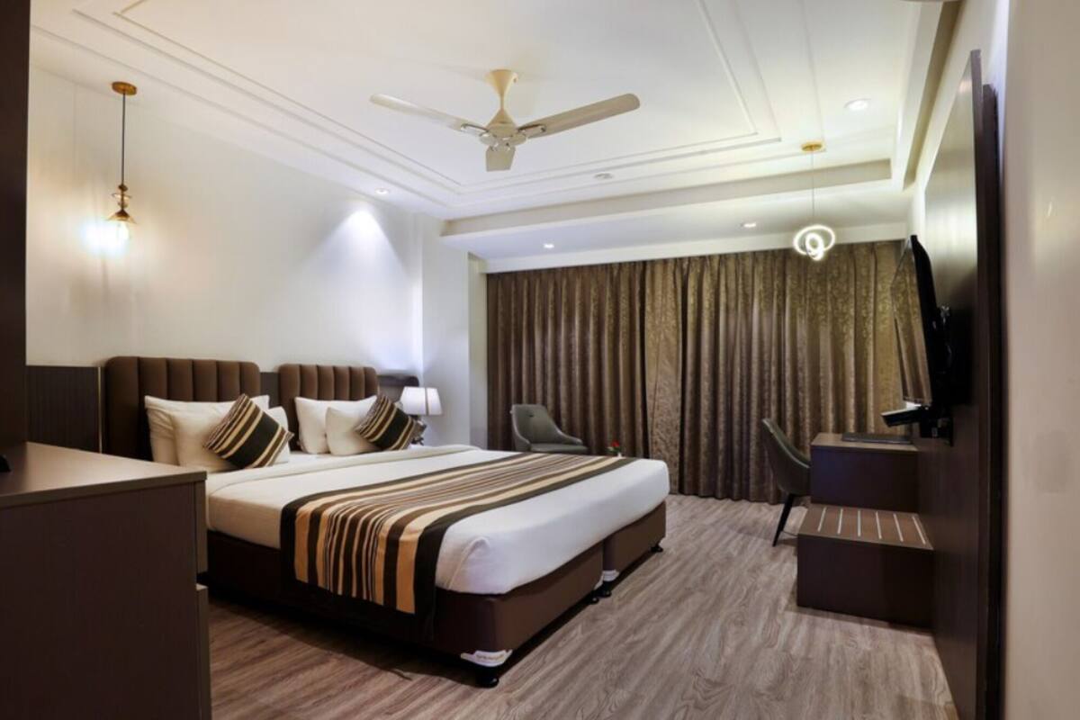A hotel room with a bed, a desk, a chair, a ceiling fan, and a TV.