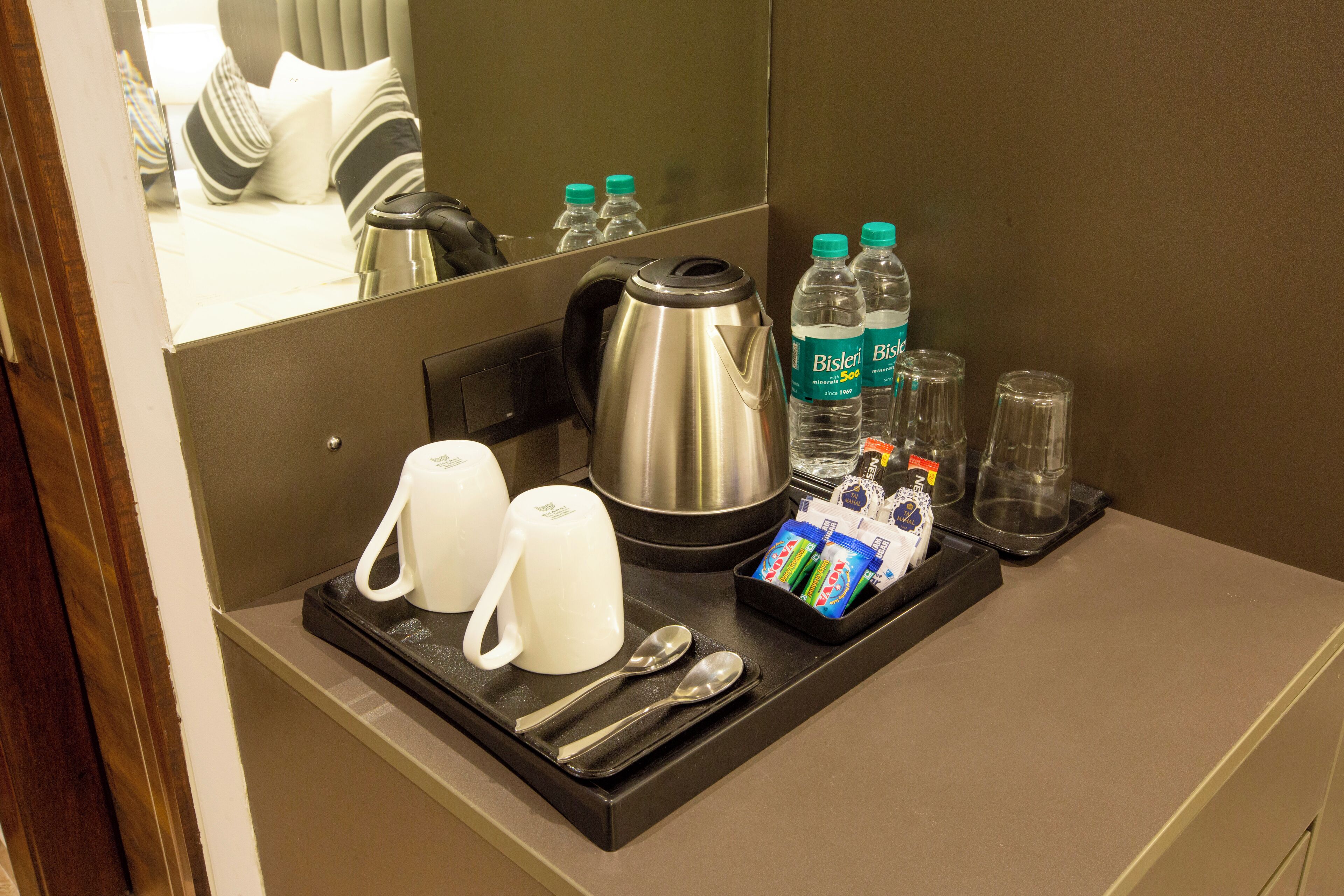 Un plateau de petit-déjeuner dans une chambre d’hôtel, avec une machine à café, deux tasses, deux cuillères, un assortiment de produits pour le petit-déjeuner et des bouteilles d’eau.