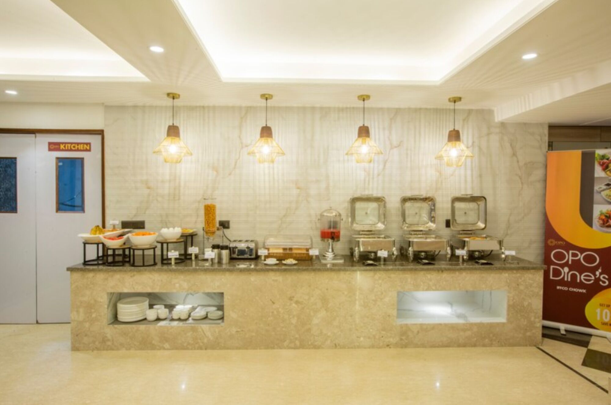 En hotellobby med en marmorskiva i receptionen, fyra hänglampor, en skylt som visar vägen till köket och en affisch som annonserar OPO Dine's.