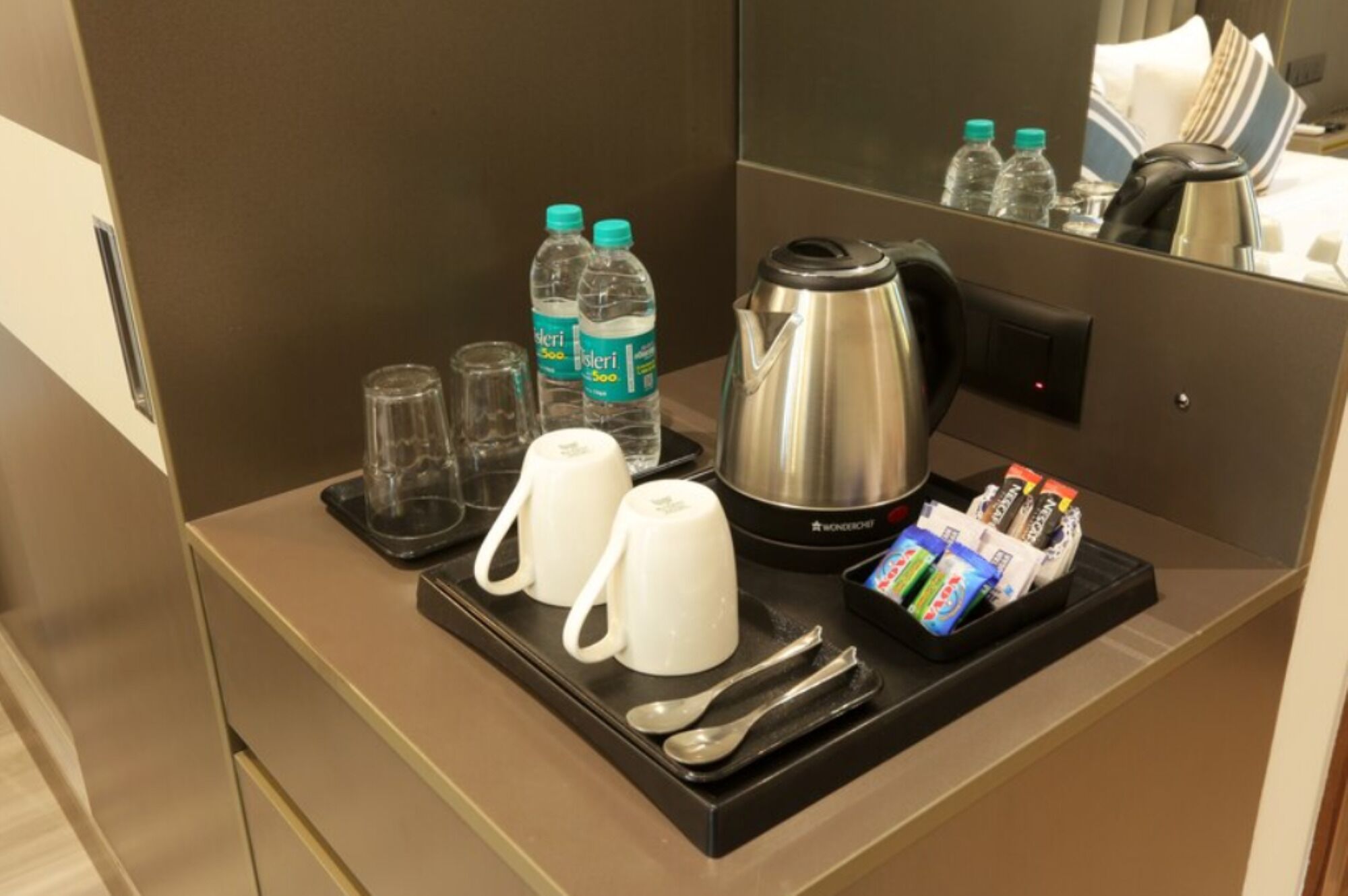 Frühstückswagen in einem Hotelzimmer mit Kaffeekocher, zwei Tassen, zwei Gläsern, einem Löffel, einer Kaffeepackung und zwei Wasserflaschen.