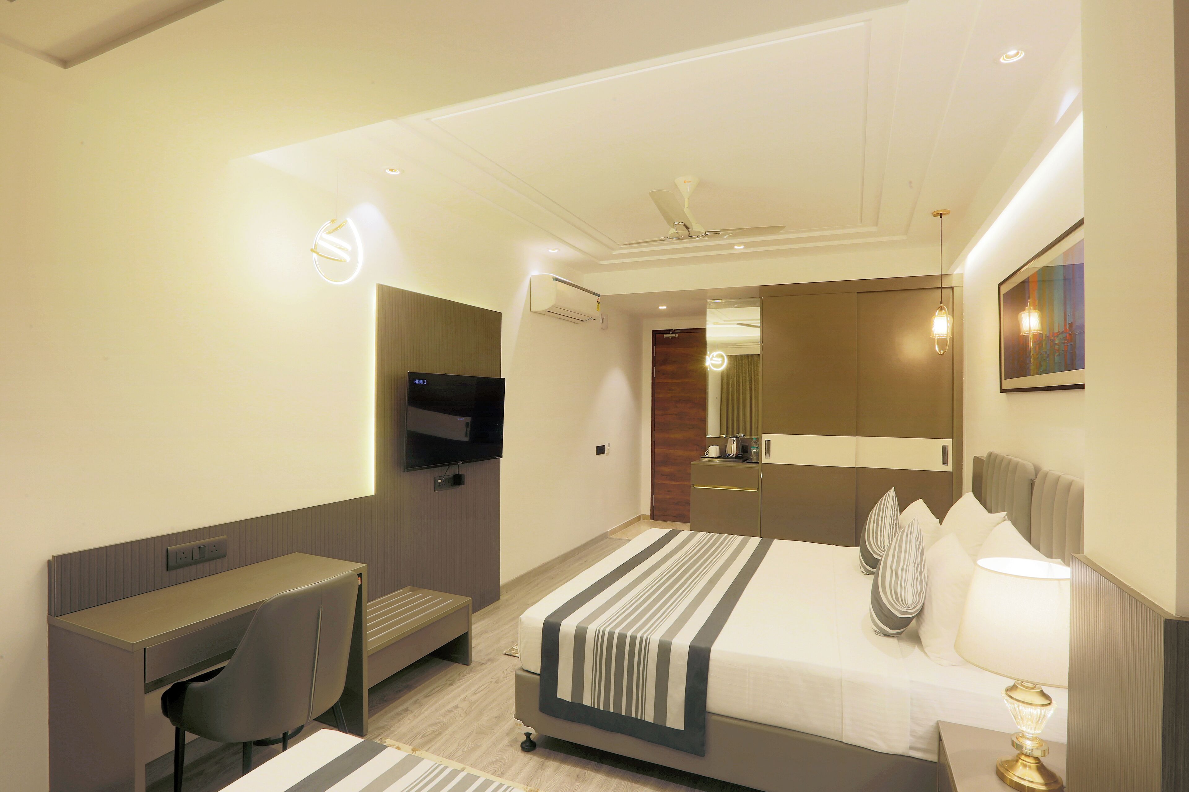 A modern hotel room with a bed, desk, chair, TV, and a mirror.
