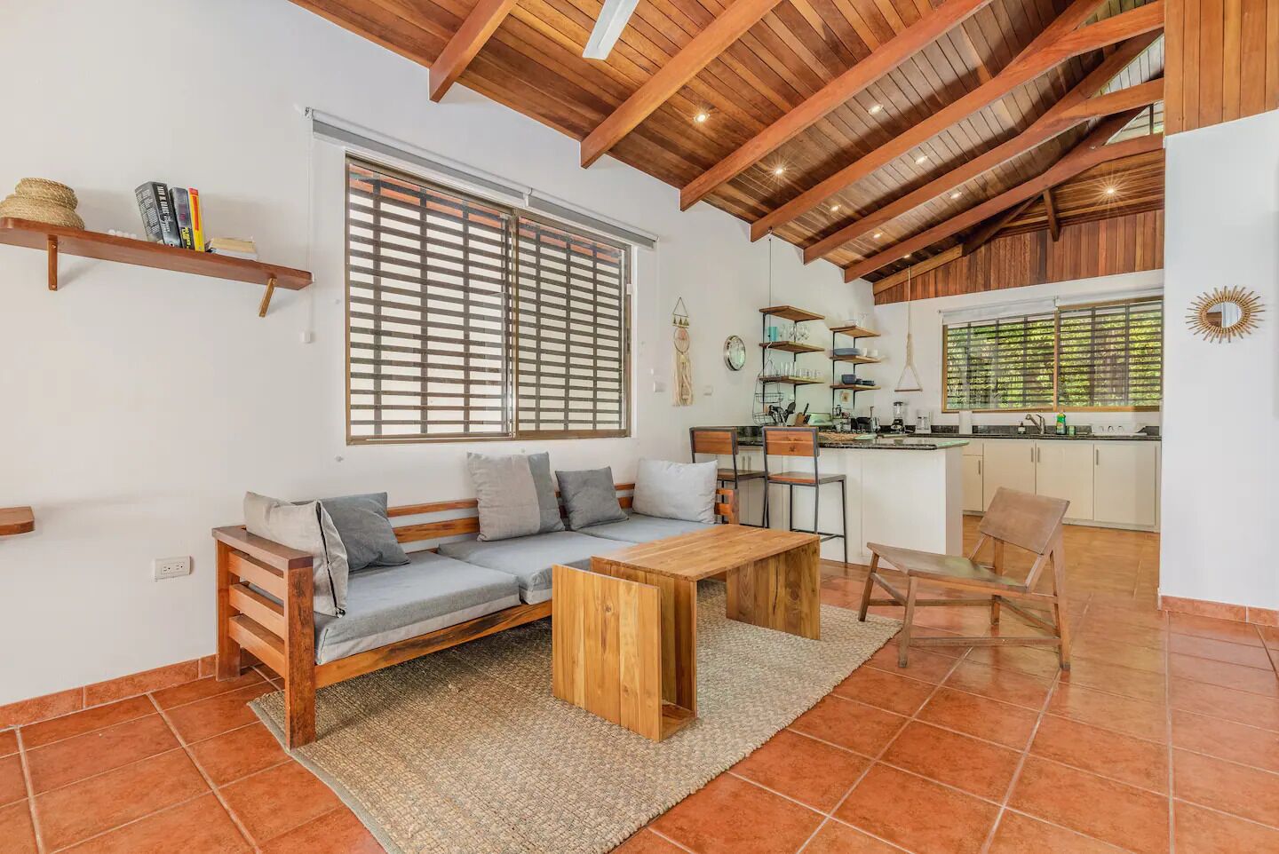 A cozy living area with a wooden ceiling, a sofa, a coffee table, and a kitchen in the background.