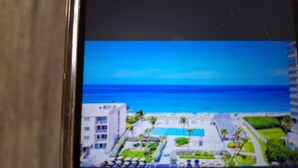 Vista de un hotel con piscina, cielo azul despejado y el océano al fondo.