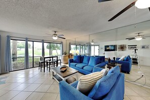 A spacious living room with a large blue sofa, a coffee table, and a dining area with chairs.