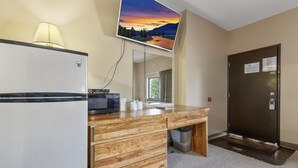 A hotel bathroom with a wooden vanity, a refrigerator, a mirror, and a door with a sign. - Commander Motel (Pequot Lakes)