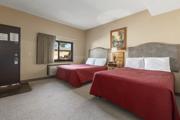 A hotel room with two beds, a window with curtains, a painting on the wall, and a door with a notice. - Commander Motel (Pequot Lakes)