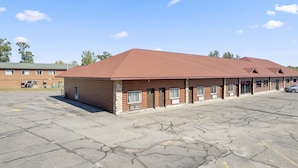 A motel with a red roof and wooden exterior, featuring a parking lot and a building in the background. - Commander Motel (Pequot Lakes)