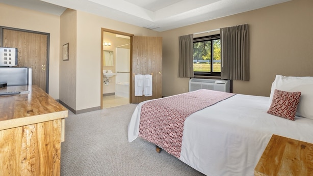 A hotel room with a bed, a desk, a bathroom, and a window with curtains. - Commander Motel (Pequot Lakes)