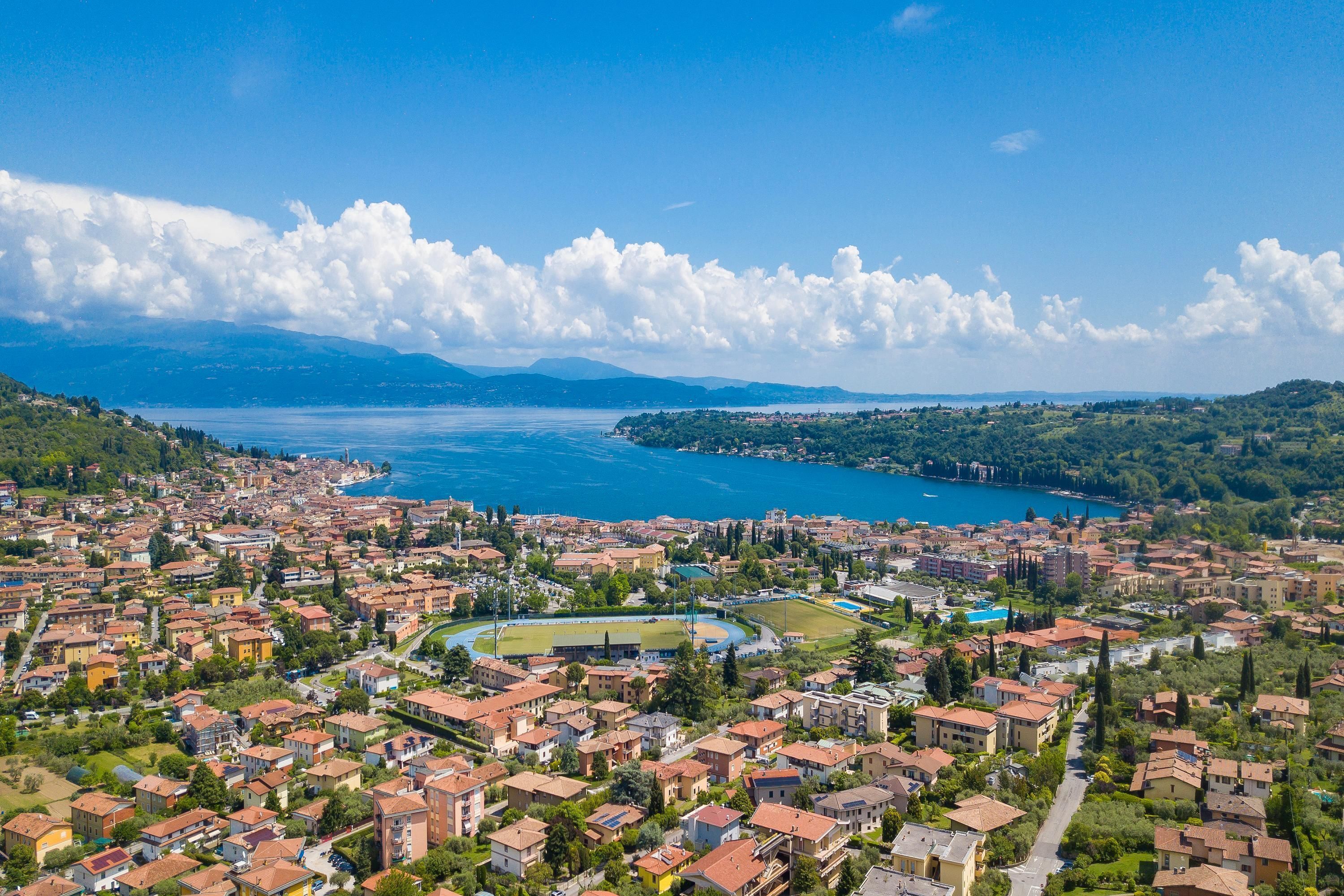 An aerial view of a coastal town with residential buildings, a sports field, and a large body of water.
